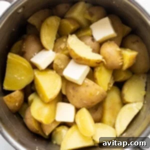 Potatoes and cheese in a pot on a white background, showing the mashing process.