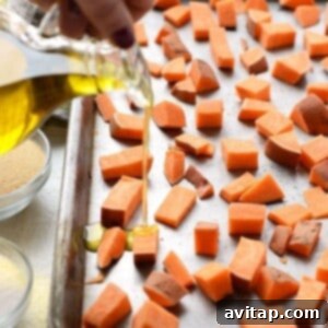 Drizzling olive oil onto sweet potato cubes on a baking sheet.