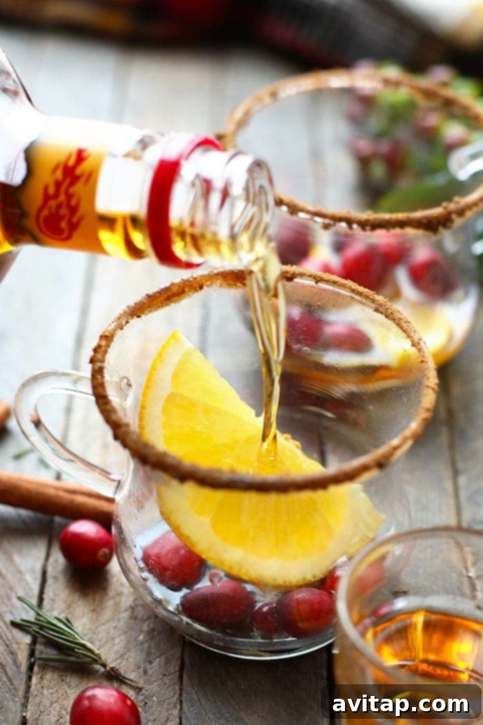 A hand pouring whiskey into a hot toddy glass, ready for the warm apple cider mixture.