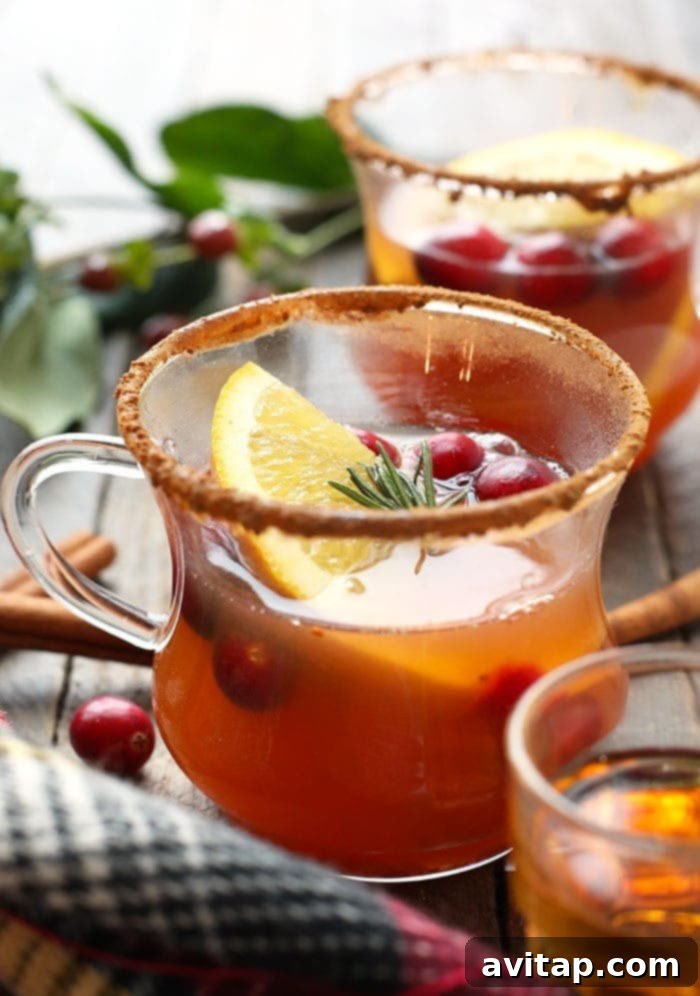 Two steaming cups of apple cider hot toddies, beautifully garnished with orange slices and rosemary, ready to be enjoyed.