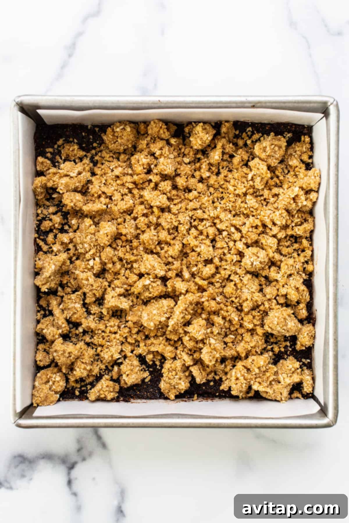 Sun-Kissed Fig & Oat Crumble Squares 5 A baking pan lined with parchment paper, filled with the bottom layer of golden-brown oat crumble crust.