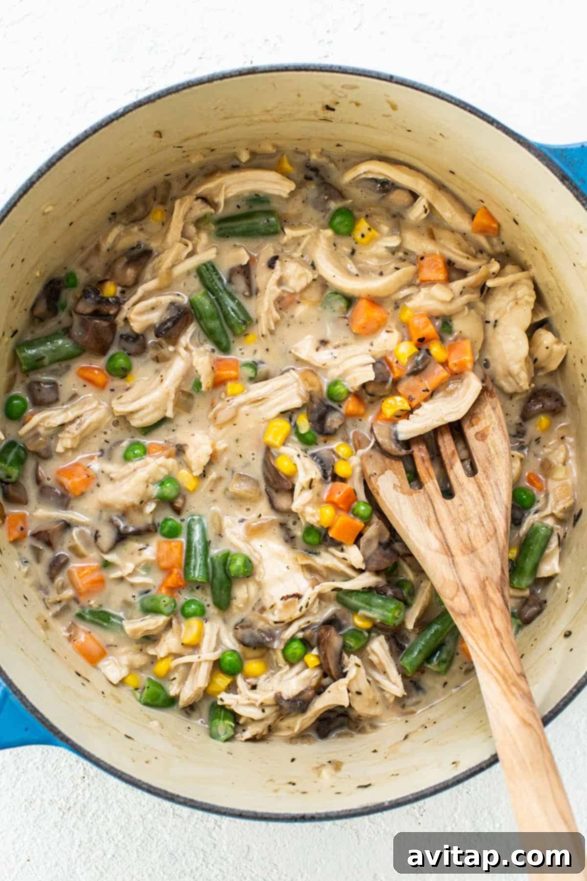 A rich chicken stew simmering in a pot with a colorful array of vegetables and a wooden spoon, indicating the preparation of a savory filling.