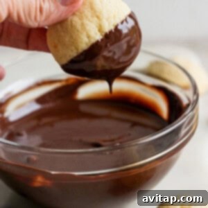 A person carefully dips a cookie into a bowl of perfectly melted chocolate, ensuring a smooth, even coating.