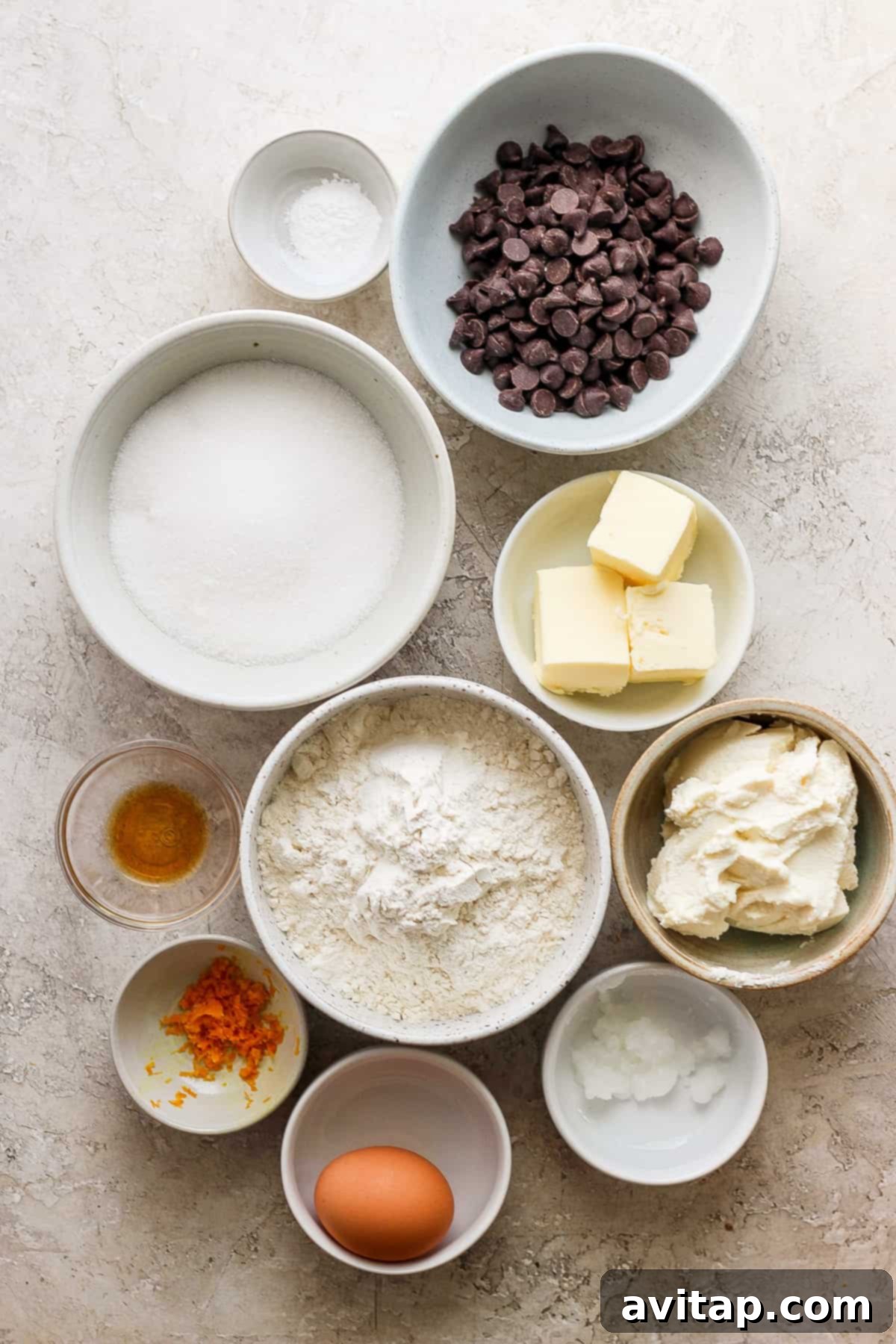Orange Kissed Chocolate Ricotta Clouds 3 A collection of baking ingredients, including flour, sugar, eggs, and citrus, neatly arranged in bowls on a wooden table.