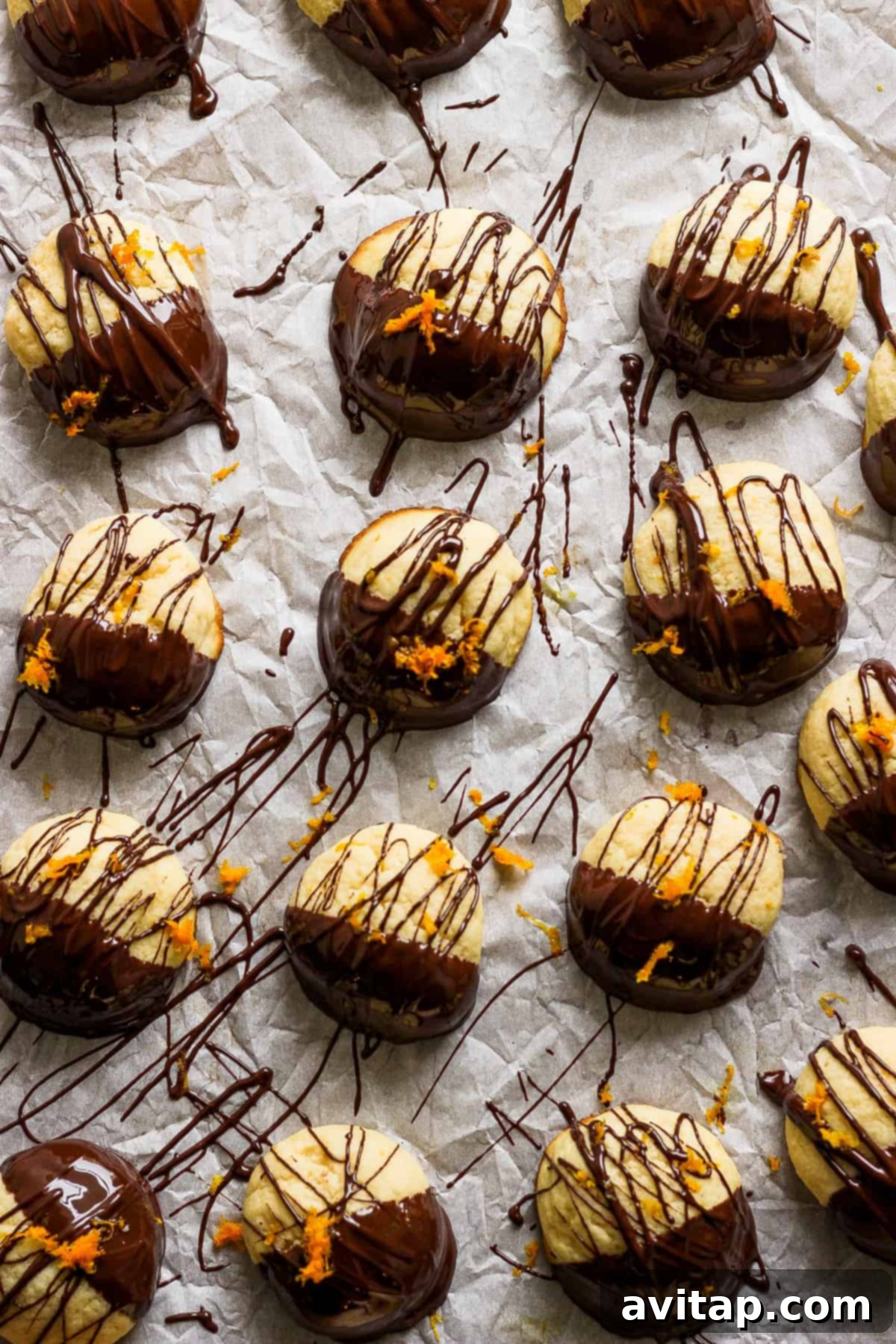 Orange Kissed Chocolate Ricotta Clouds 6 A festive display of chocolate-covered ricotta cookies adorned with bright orange zest, arranged on parchment paper.
