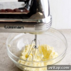 A person expertly mixing softened butter and sugar in a bowl with a hand mixer, creating a light and fluffy base for the cookies.