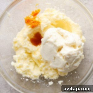 A bowl of creamy, mixed wet ingredients, including ricotta and orange zest, showing the smooth consistency before adding the egg.
