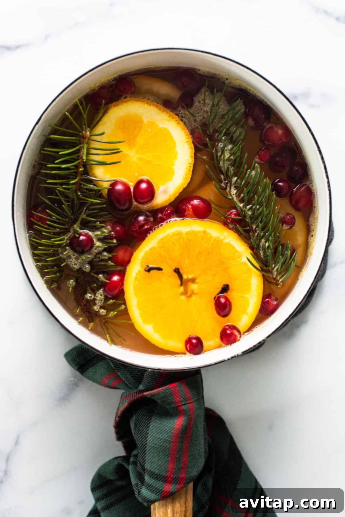 A pan with sliced oranges, vibrant red cranberries, and fragrant sprigs of fir simmering gently on a stovetop, filling the air with a festive aroma.