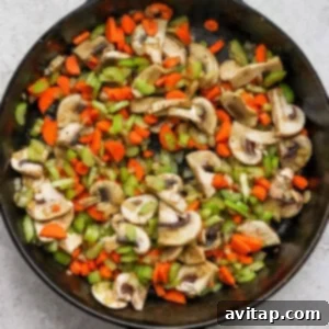 A skillet filled with sautéing mushrooms, carrots, and celery, deglazed with white wine.