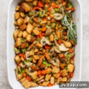 A white baking dish filled with stuffing ingredients and vegetables, with a herb bundle nestled within.