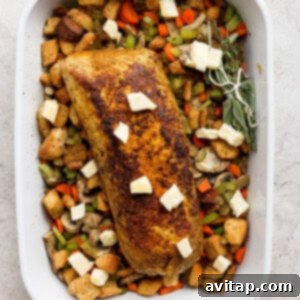 A white baking dish with a roasted pork tenderloin resting on a bed of stuffing and vegetables, topped with butter.