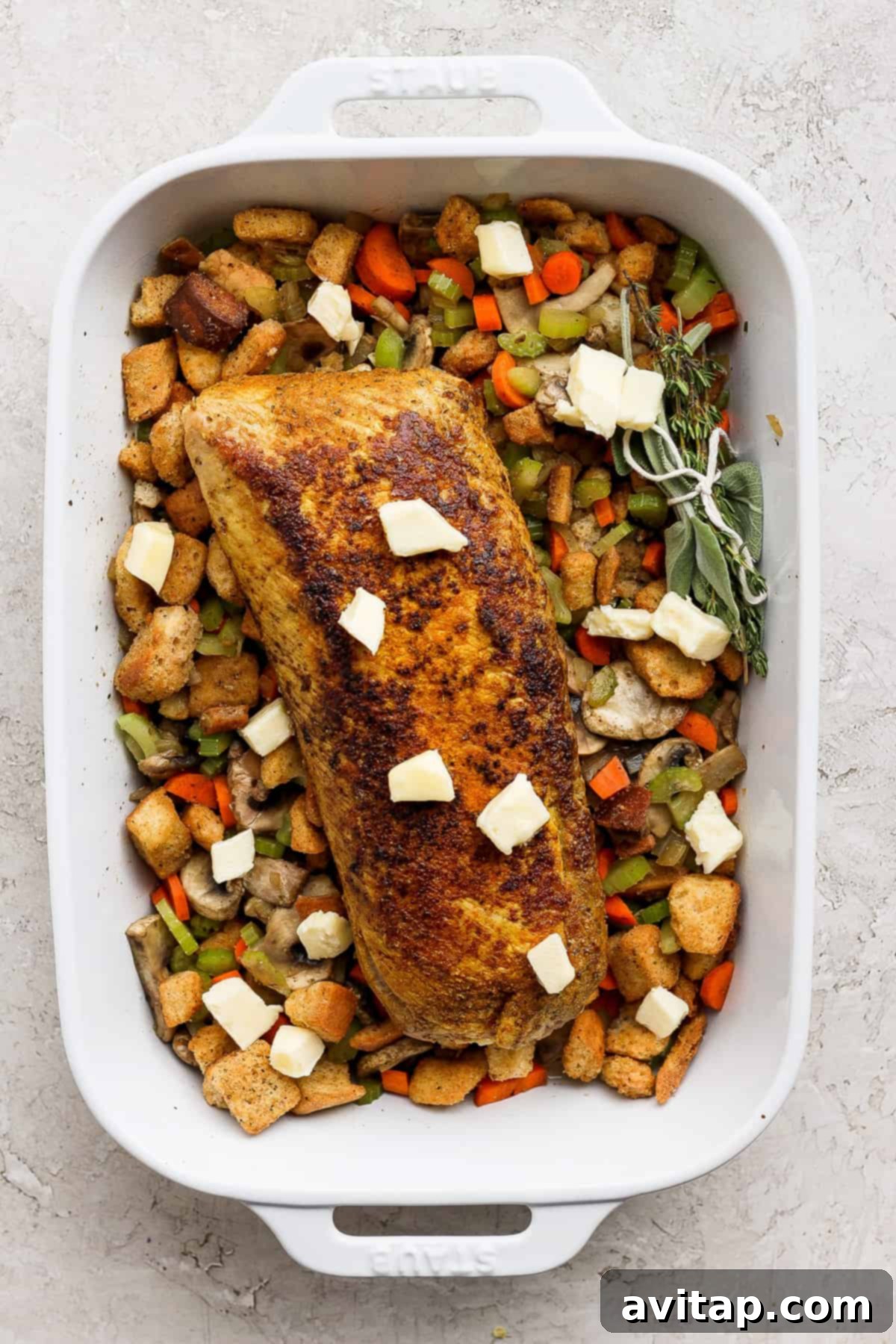 A white baking dish filled with a beautifully roasted pork tenderloin nestled atop a bed of savory mushroom stuffing and vegetables, ready for resting.