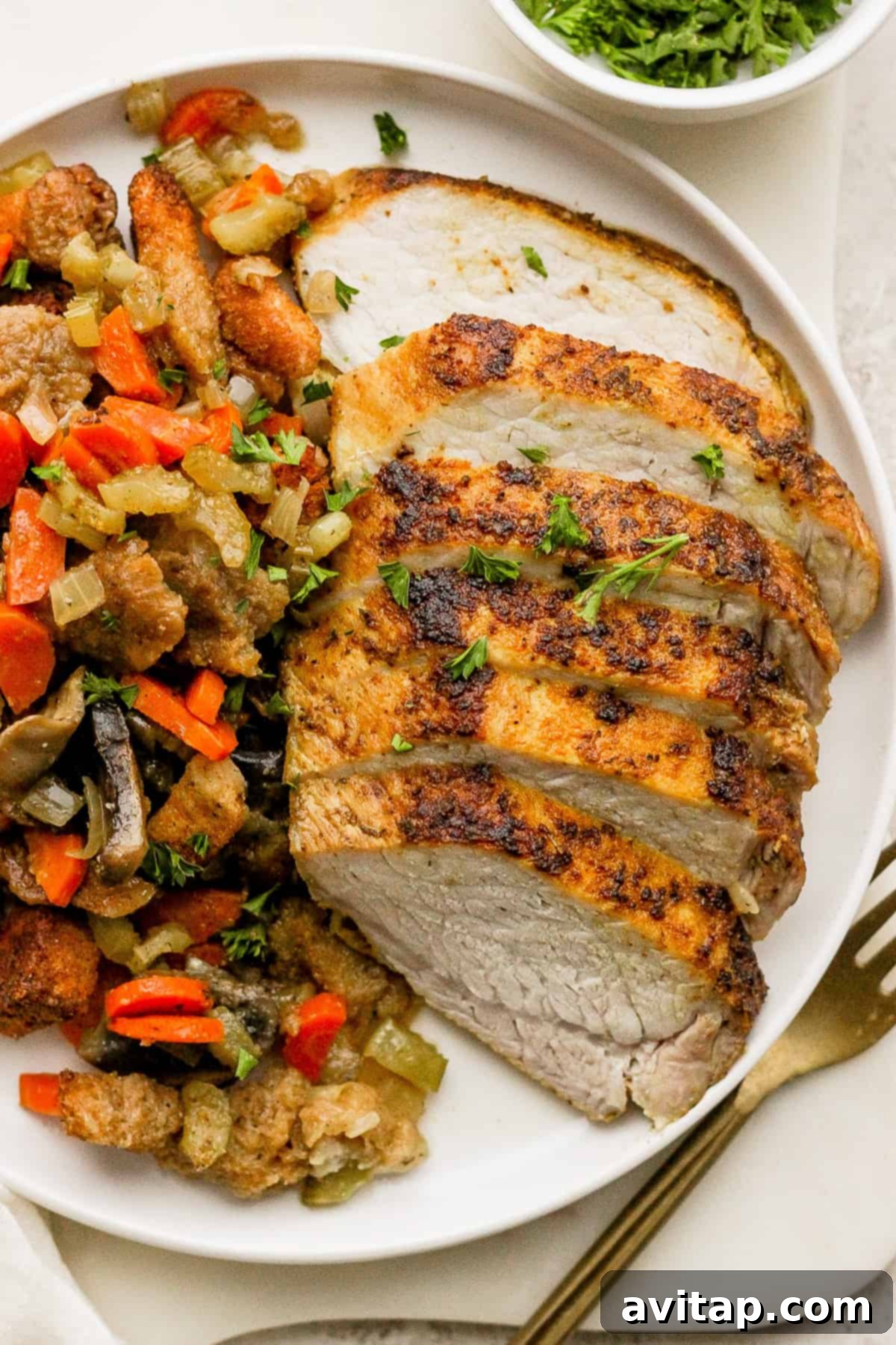 A festive plate featuring expertly sliced roasted pork tenderloin, accompanied by a hearty portion of mushroom stuffing and vibrant roasted vegetables, ready to be served.