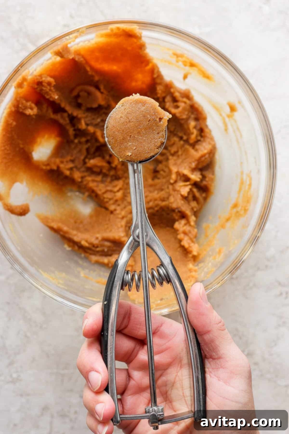 A person holding a hand mixer over a bowl of peanut butter.