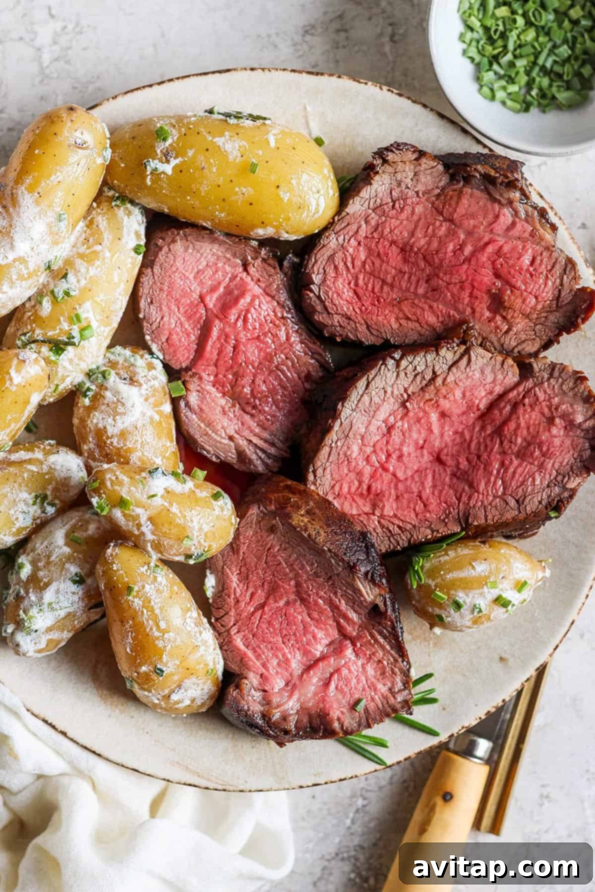 A beautifully plated seared beef tenderloin roast with golden roasted fingerling potatoes and fresh herbs, ready to be enjoyed.