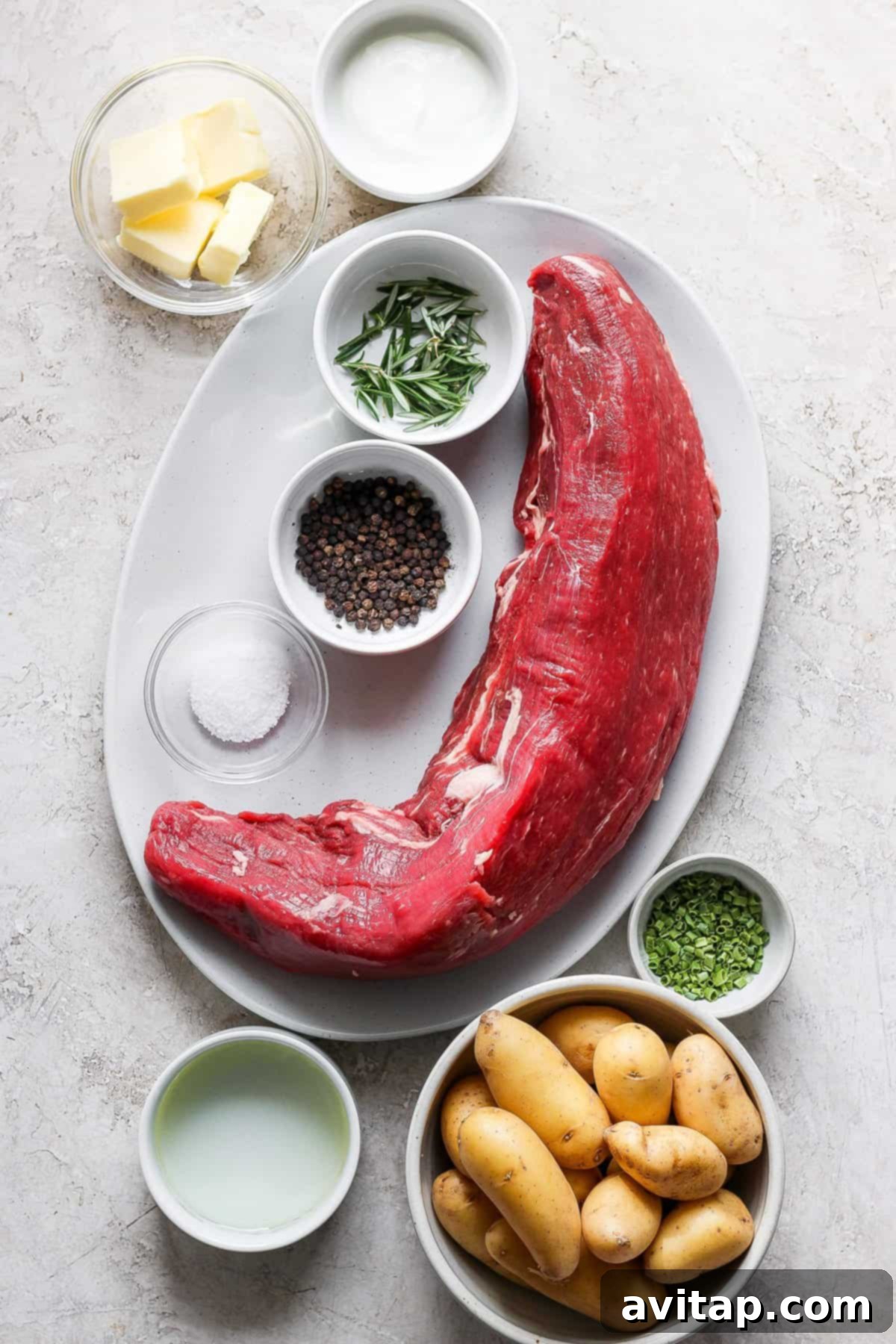 A meticulously arranged plate featuring a sliced seared beef tenderloin alongside creamy roasted fingerling potatoes, garnished with fresh herbs and a savory sauce.