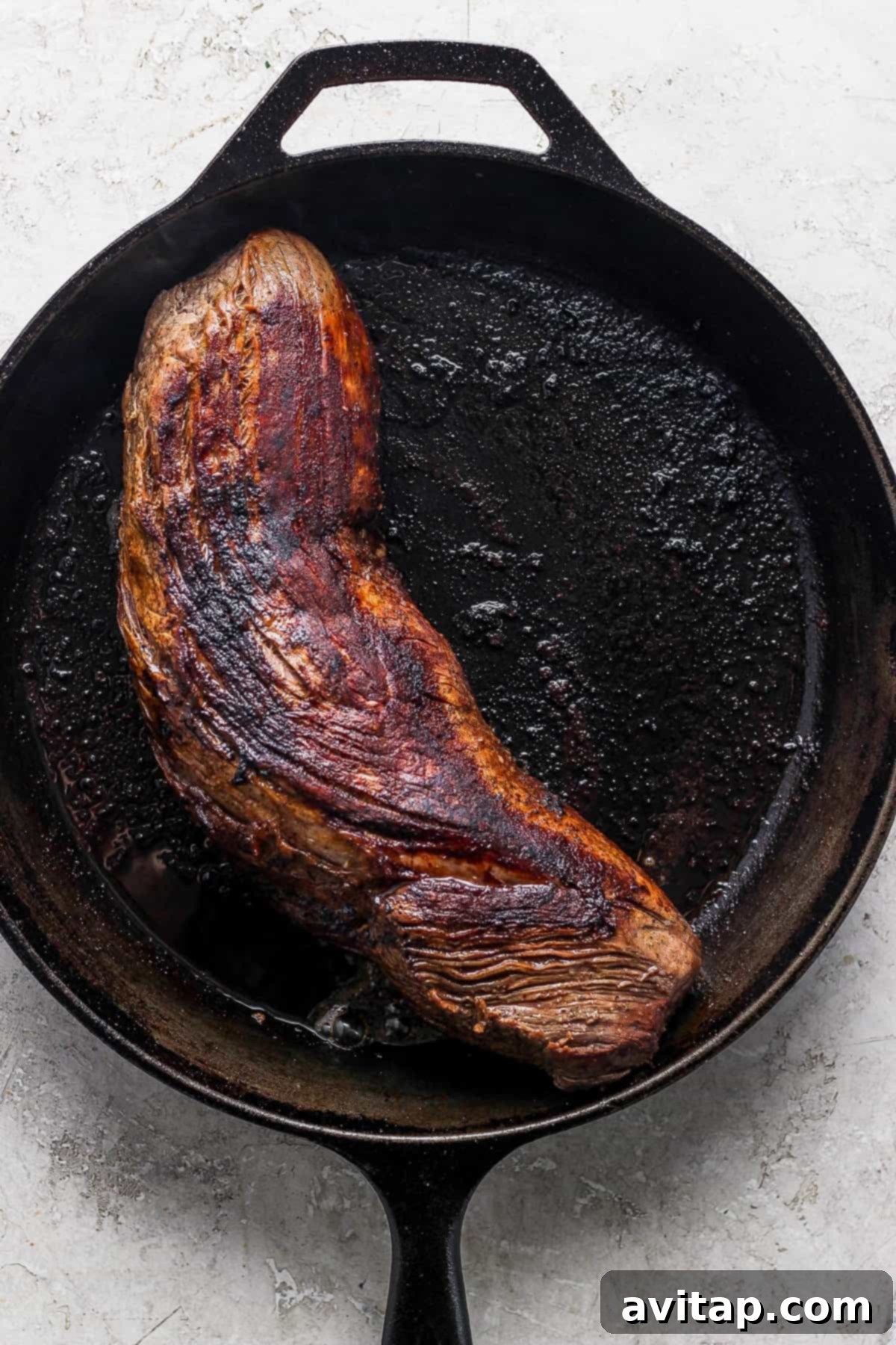 A large cut of beef tenderloin sizzling in a hot cast iron skillet, developing a rich, dark crust during the searing process.