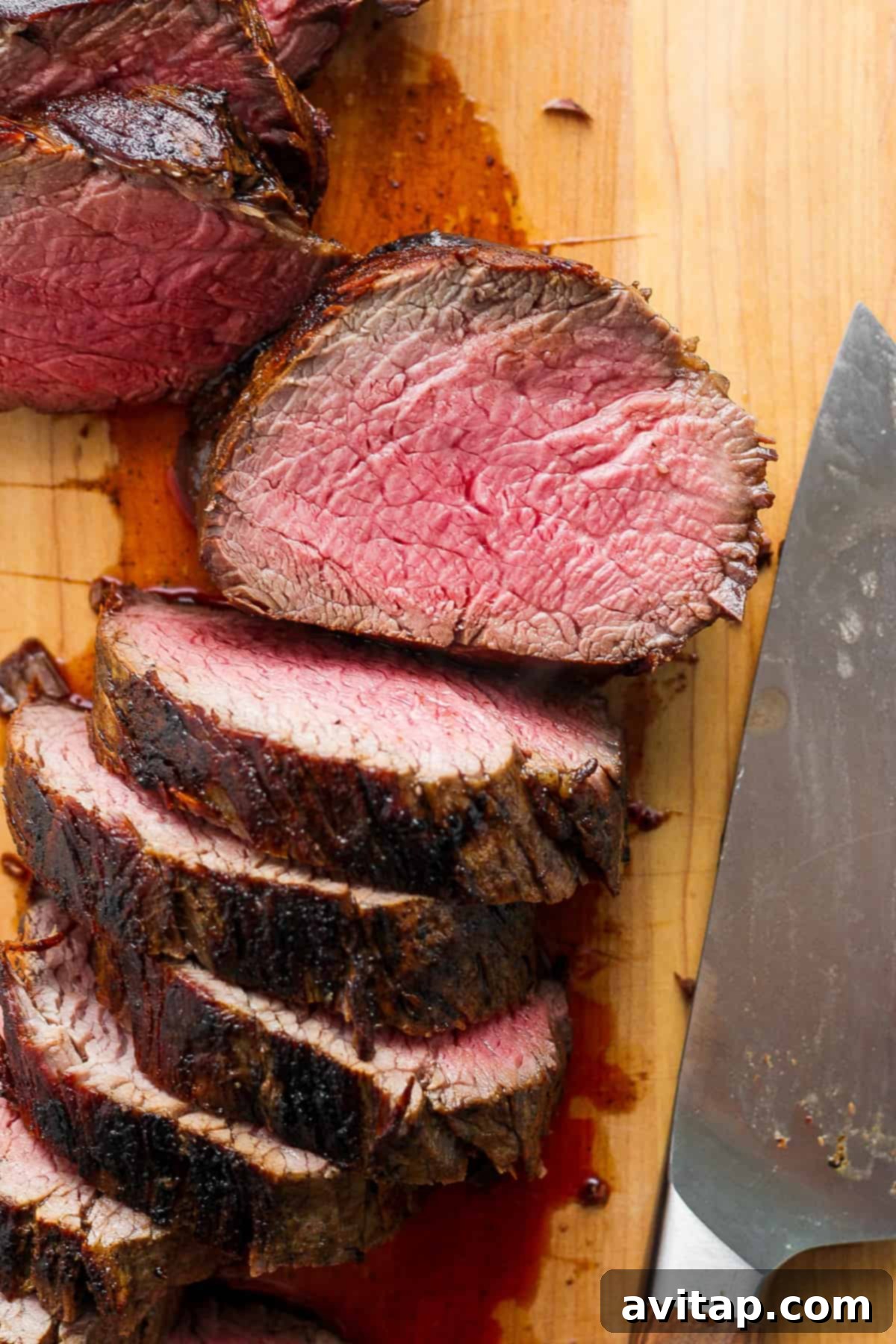 Expertly sliced medium-rare beef tenderloin rounds displayed on a wooden cutting board, alongside a sharp carving knife, highlighting the juicy, tender interior.