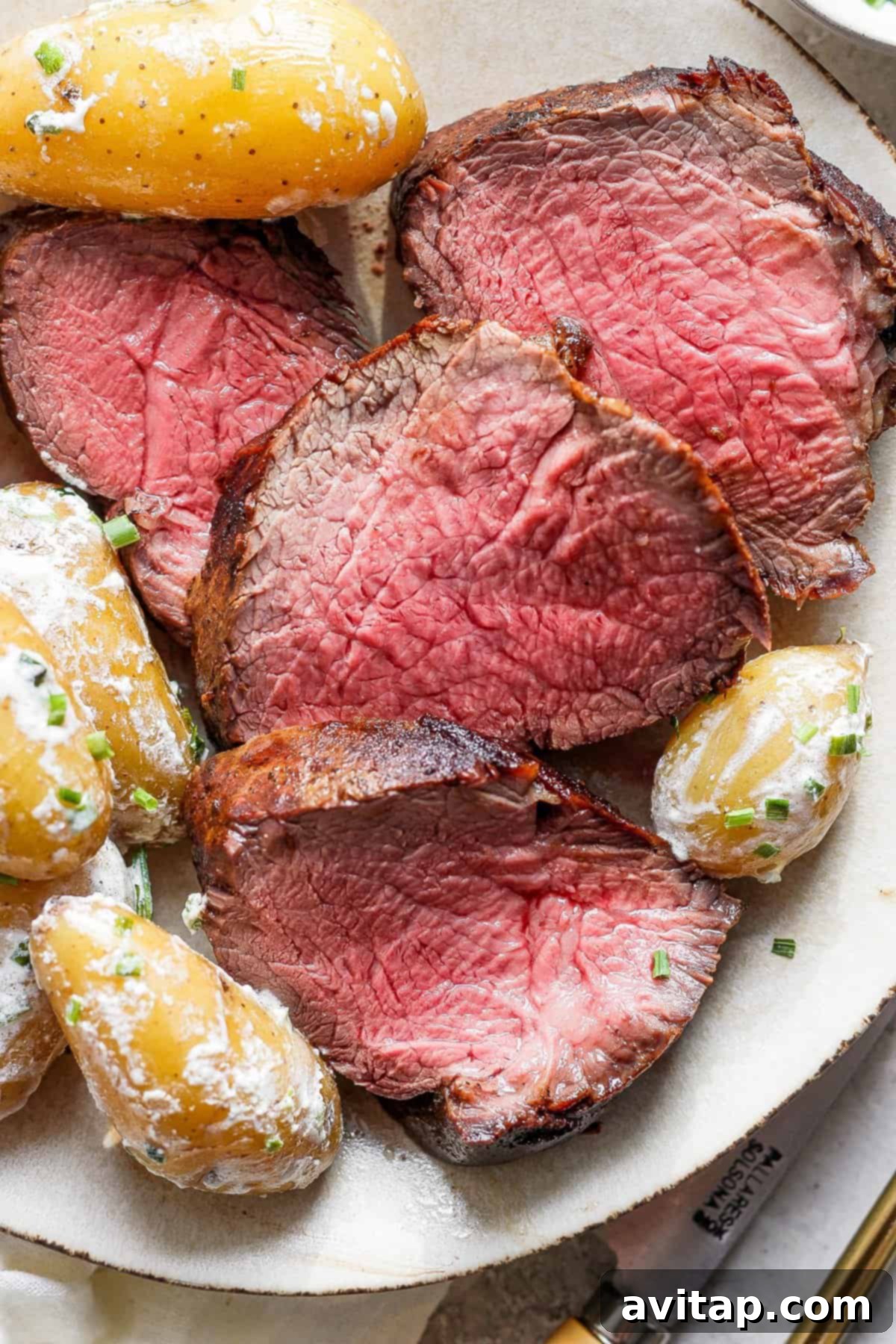A close-up shot of a plate with a generous portion of seared beef tenderloin and creamy fingerling potatoes, garnished with fresh herbs, inviting to be eaten.