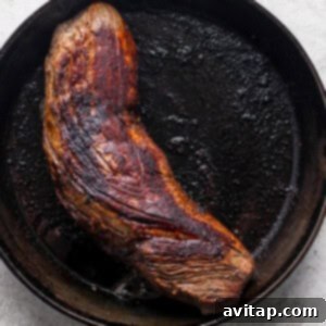 A beef tenderloin being expertly seared in a cast iron skillet, developing a dark, crispy crust.