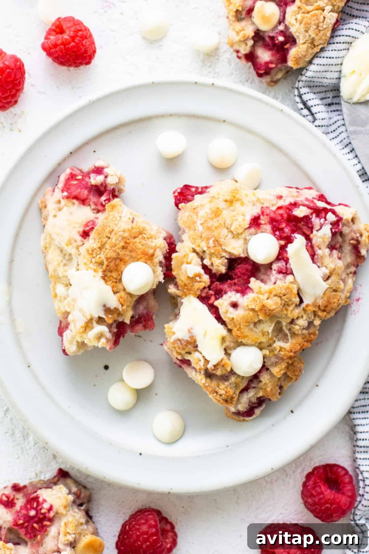 A stack of white chocolate raspberry scones on a white plate, ready to be served with a cup of coffee.