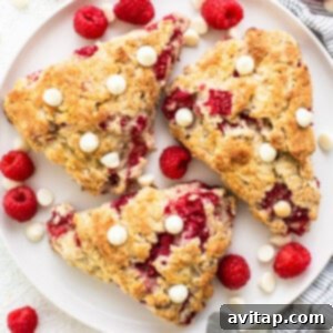 A beautifully plated scone, generously studded with raspberries and white chocolate, signifying a delicious breakfast.