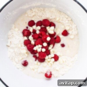 A mixing bowl containing scone dough with raspberries and white chocolate chips, ready for shaping.
