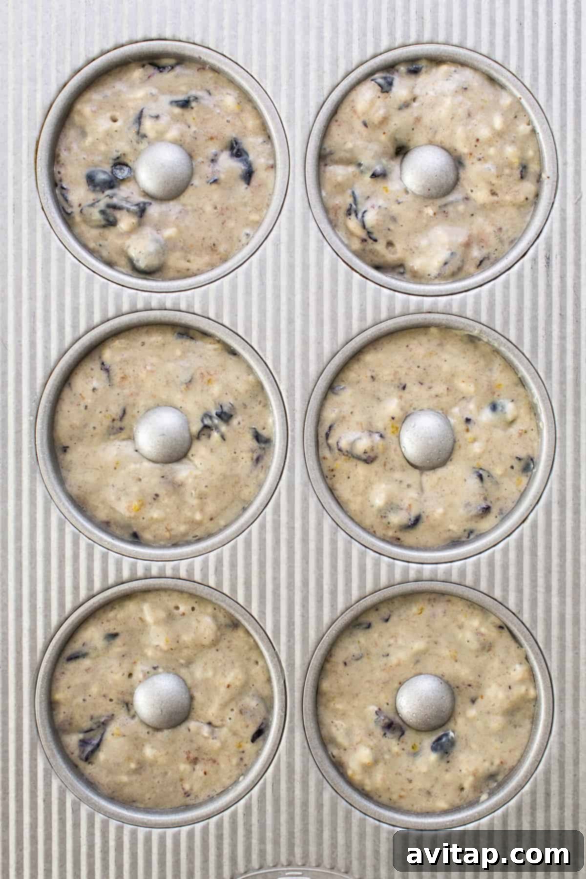 A muffin tin filled with blueberry protein muffin batter, ready for baking.