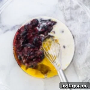 A bowl with berries and eggs in it, showing wet ingredients being mixed.