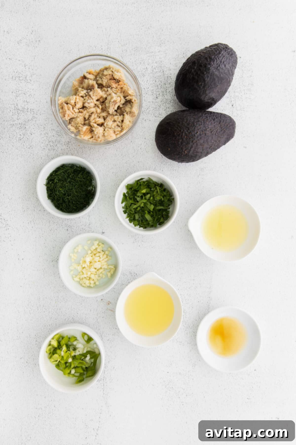 A vibrant collection of all the fresh ingredients destined for the stuffed avocado boats, neatly arranged in small, individual bowls on a rustic wooden surface.