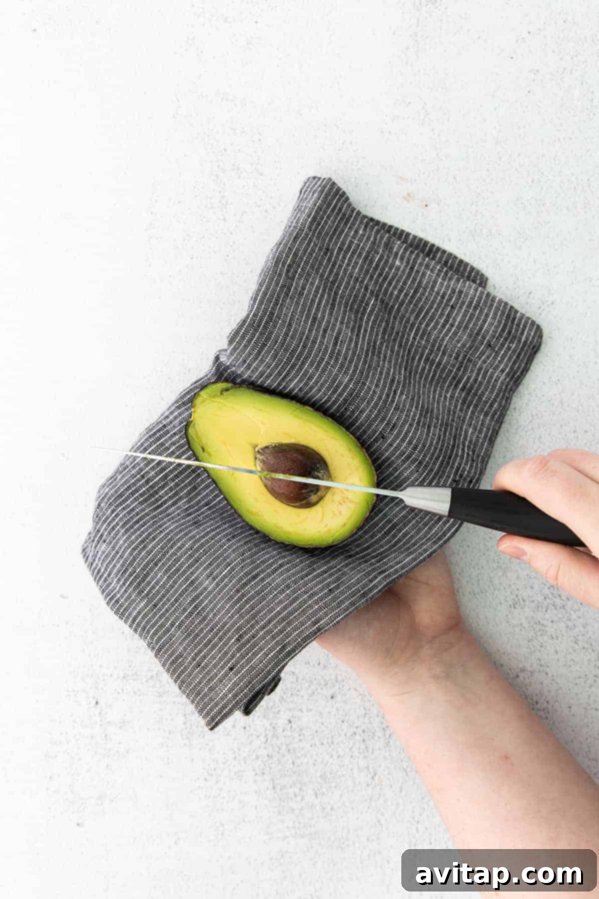 A close-up demonstration of carefully removing the pit from a perfectly ripe avocado using a sharp kitchen knife.