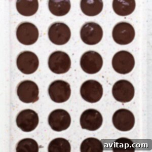 A tray filled with chocolate covered donuts, illustrating the process of topping the cookie dough cups with melted chocolate for a smooth, glossy finish.