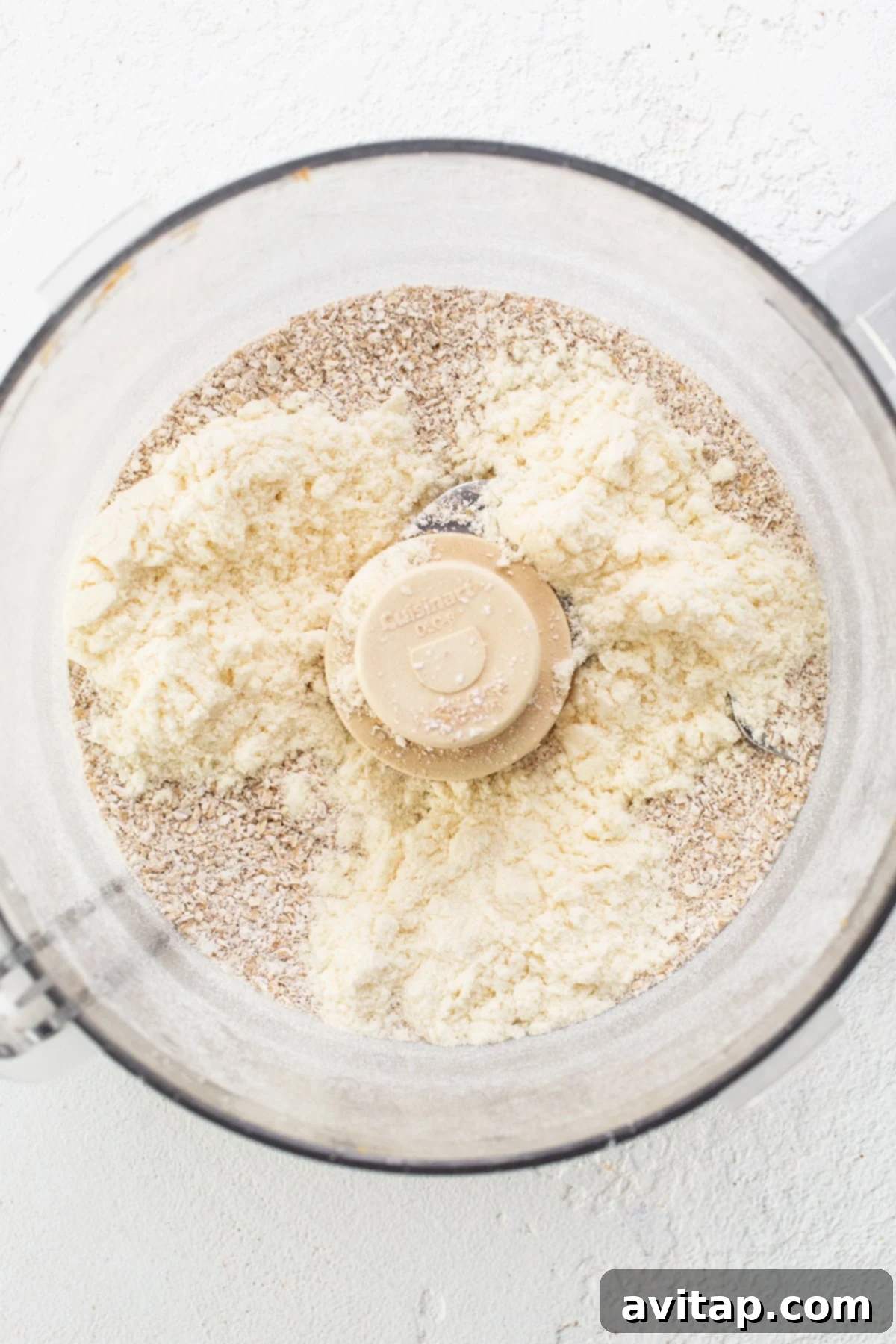 A food processor bowl filled with finely ground oat flour and other dry ingredients, ready for mixing.