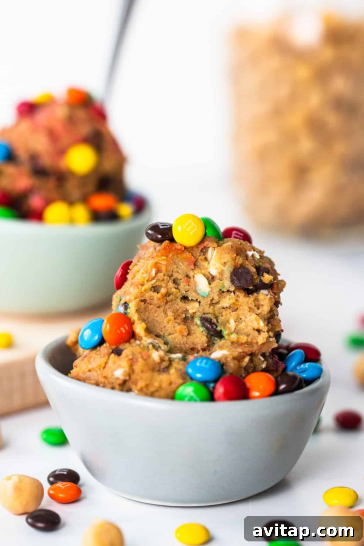Protein Packed Monster Cookie Dough 2 A bowl brimming with creamy protein monster cookie dough, adorned with an generous amount of mini chocolate chips and colorful M&M's, inviting you to take a spoonful.