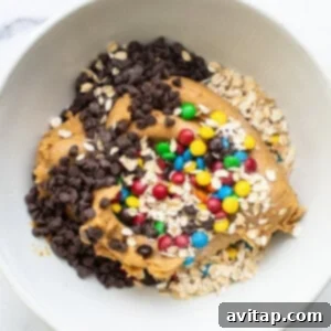 Protein Packed Monster Cookie Dough 10 A white bowl filled with a blend of granola, oats, and chocolate chips, ready to be added to the cookie dough mixture.