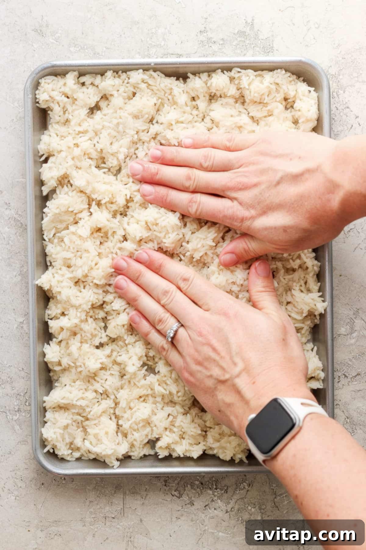 A close-up shot of hands pressing sticky rice onto a baking sheet, preparing it for crisping.