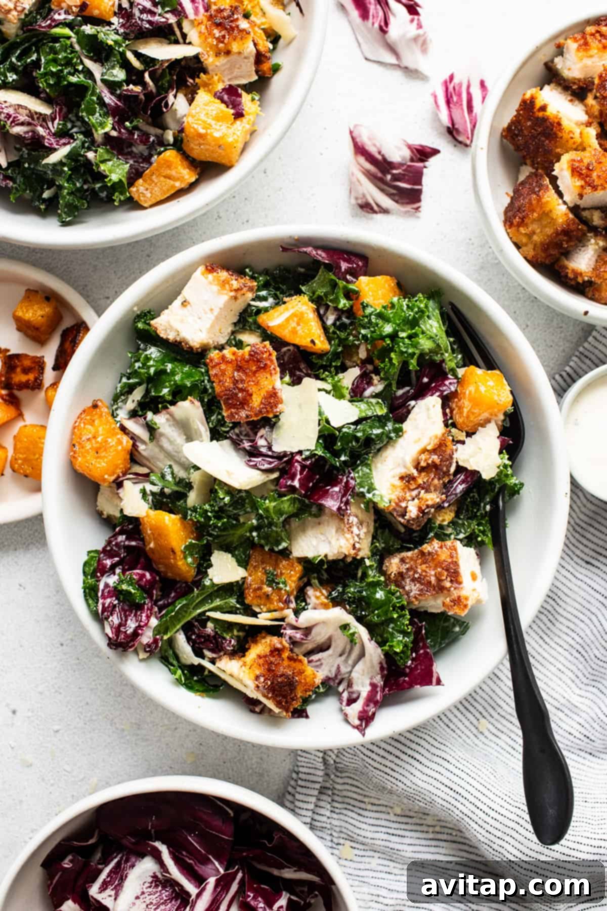 A vibrant bowl of crispy chicken kale caesar salad, showcasing golden chicken pieces, green kale, orange butternut squash, and a creamy dressing.