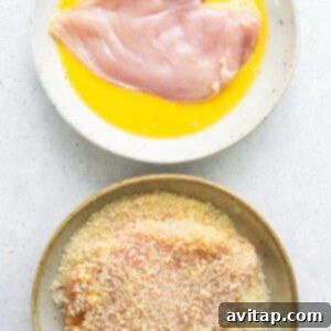 Two bowls with chicken breasts ready for breading, and a bowl of whisked eggs, and another of panko and Parmesan.