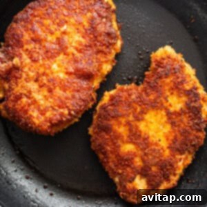Two golden-brown fried chicken patties sizzling in a frying pan.