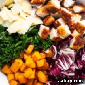 A bowl filled with massaged kale, diced crispy chicken, roasted butternut squash, and shaved Parmesan cheese.