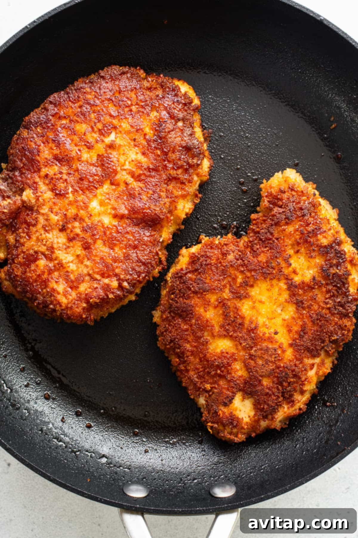 Two golden-brown, crispy fried chicken patties sizzling in a cast iron frying pan.