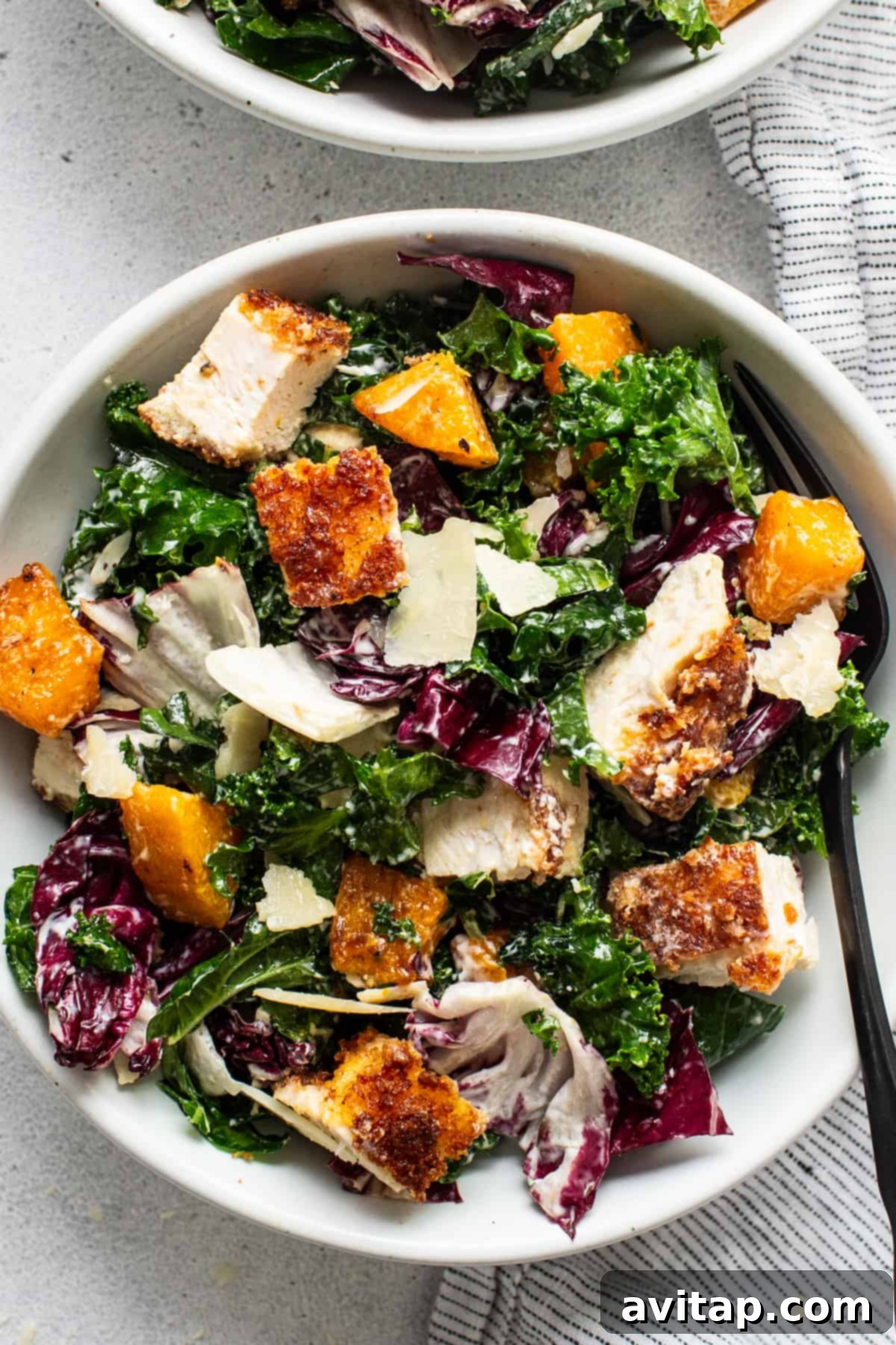 Two bowls of crispy chicken kale caesar salad, artfully arranged with Parmesan shavings and dressing.