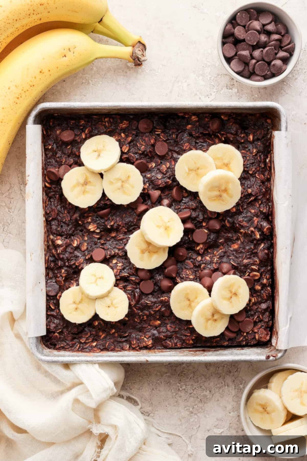 A baking pan filled with golden-brown chocolate banana baked oatmeal, topped with fresh banana slices and melted chocolate chips, ready to be served.