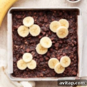A baking pan filled with golden-brown chocolate banana baked oatmeal, topped with fresh banana slices and melted chocolate chips, ready to be served.