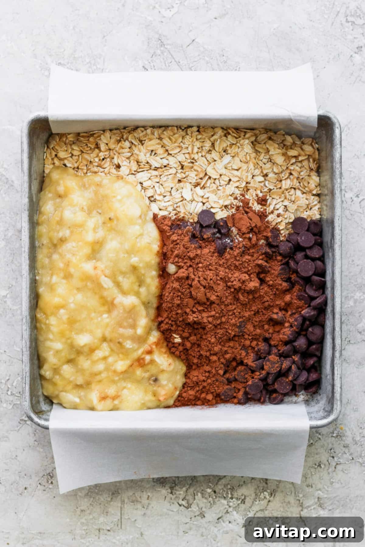 A deep baking dish filled with unbaked ingredients for chocolate banana oatmeal, featuring rolled oats, mashed bananas, and chocolate chips waiting to be mixed.