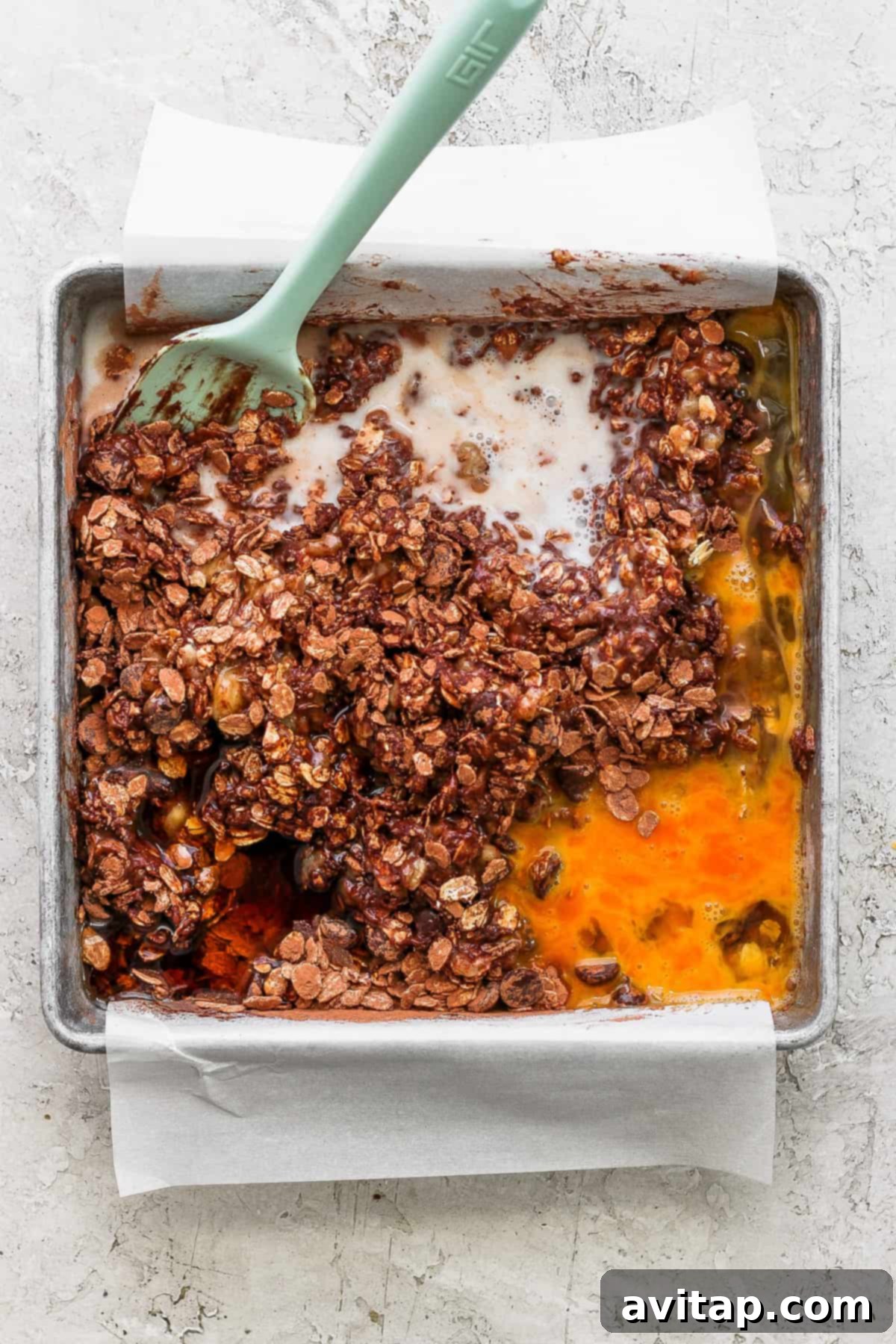 A baking pan containing unbaked chocolate banana oatmeal mixture, with a scoop removed to show the rich texture.
