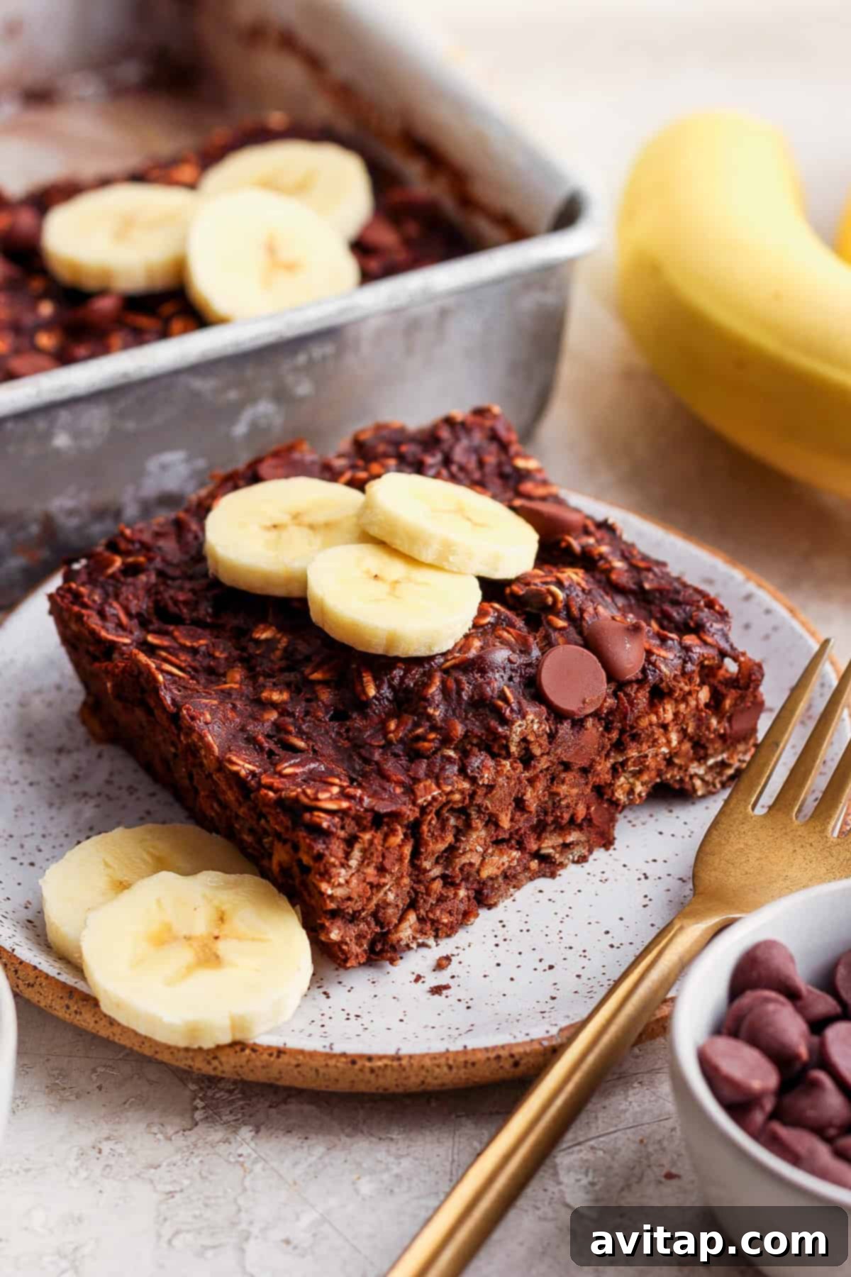 Sliced chocolate banana baked oatmeal bars arranged on a white plate with fresh banana slices on the side.
