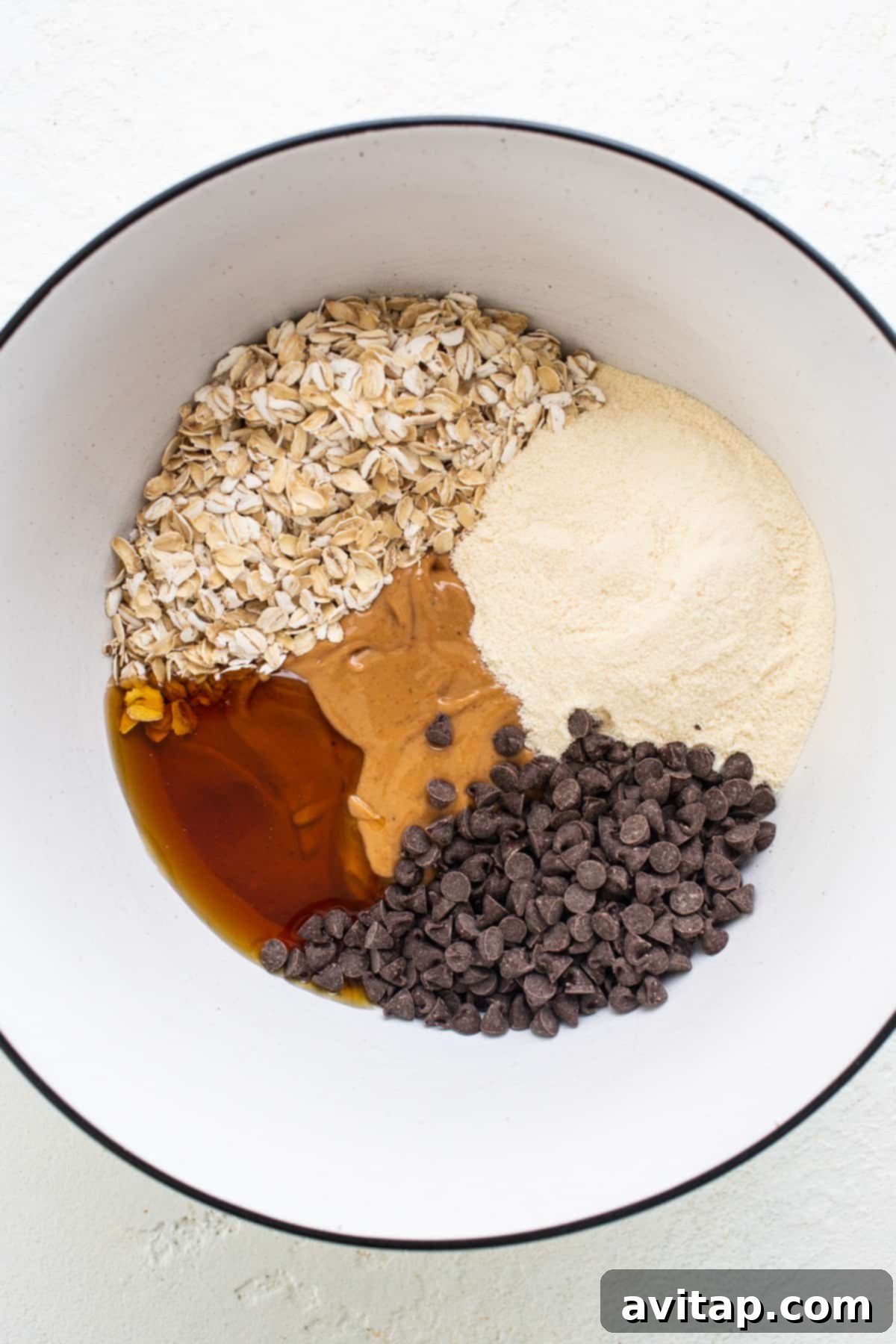 A rustic bowl filled with protein cookie dough ingredients including oats, protein powder, and cashew butter, ready for mixing.