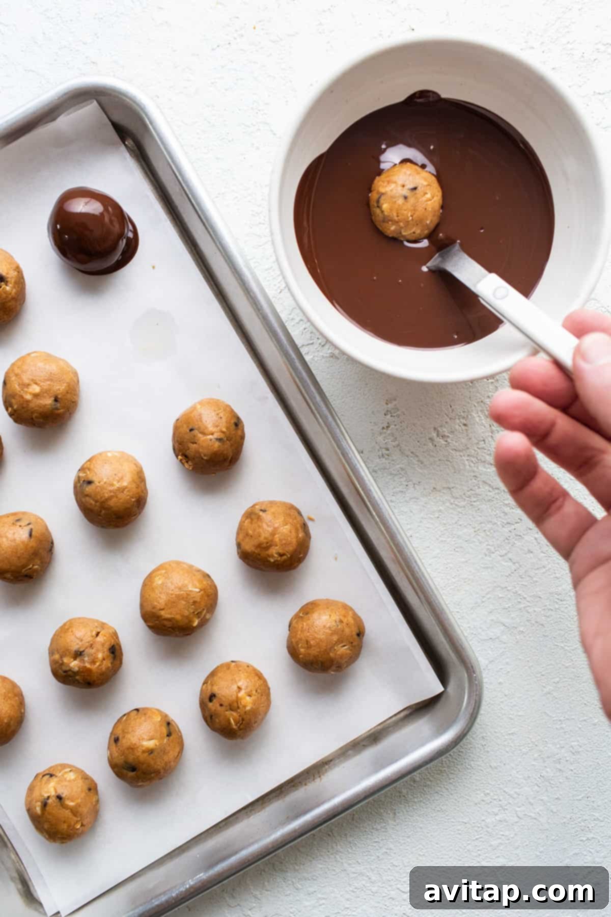 Melted chocolate being drizzled over a tray of truffles, showcasing the coating process.