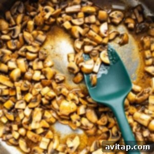 Sautéing mushrooms in a pan with a green spatula.